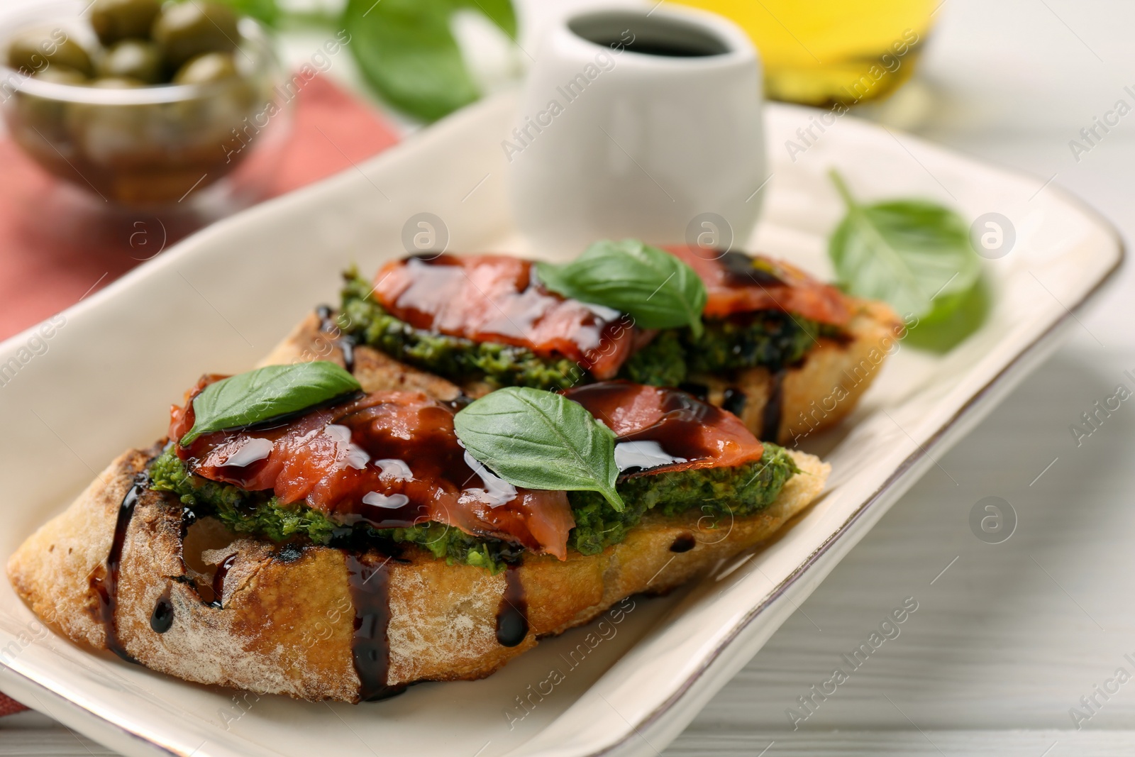 Photo of Delicious bruschettas with balsamic vinegar and toppings on white wooden table, closeup