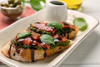 Delicious bruschettas with balsamic vinegar and toppings on white wooden table, closeup