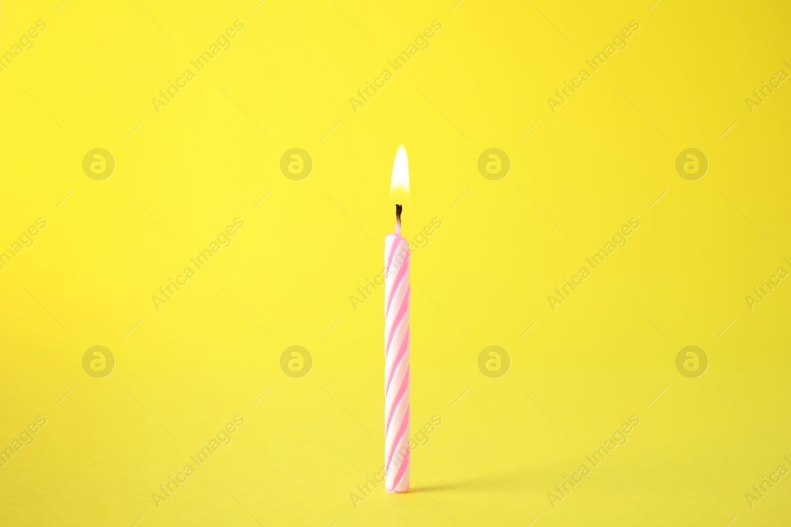 Photo of Burning pink striped birthday candle on yellow background