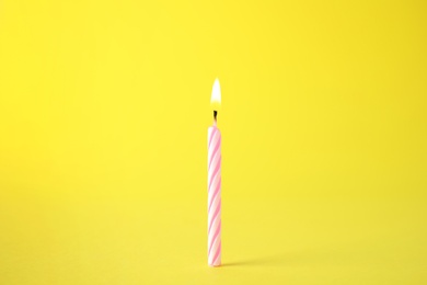Photo of Burning pink striped birthday candle on yellow background