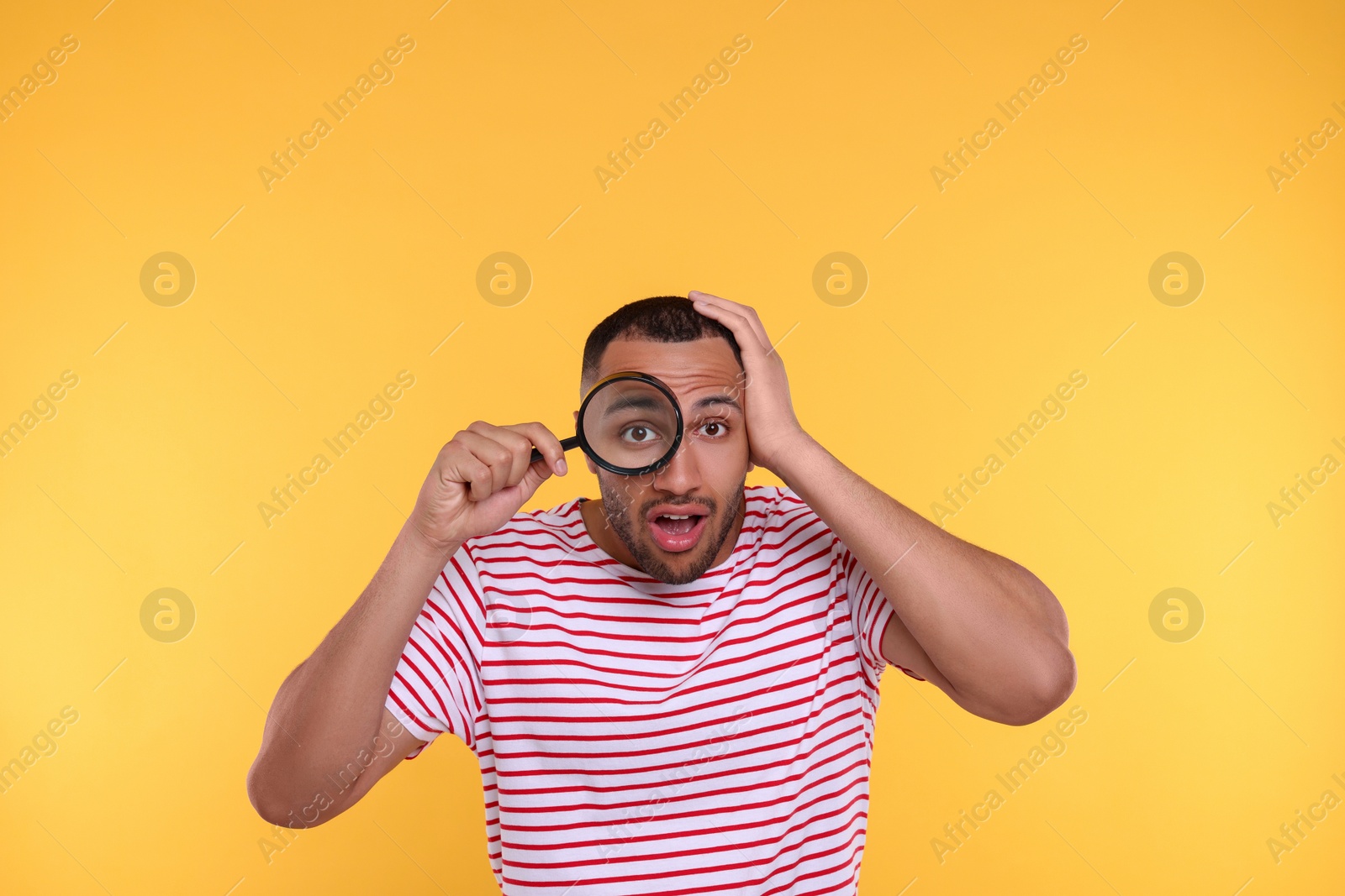 Photo of Shocked man looking through magnifier glass on orange background