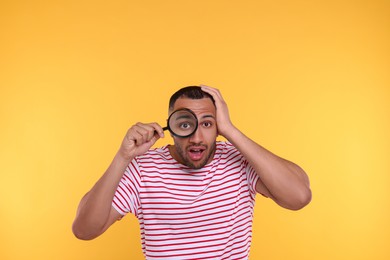 Photo of Shocked man looking through magnifier glass on orange background