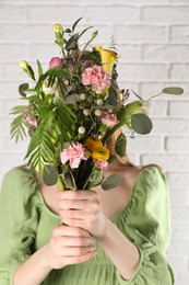 Woman covering her face with beautiful spring bouquet near white brick wall