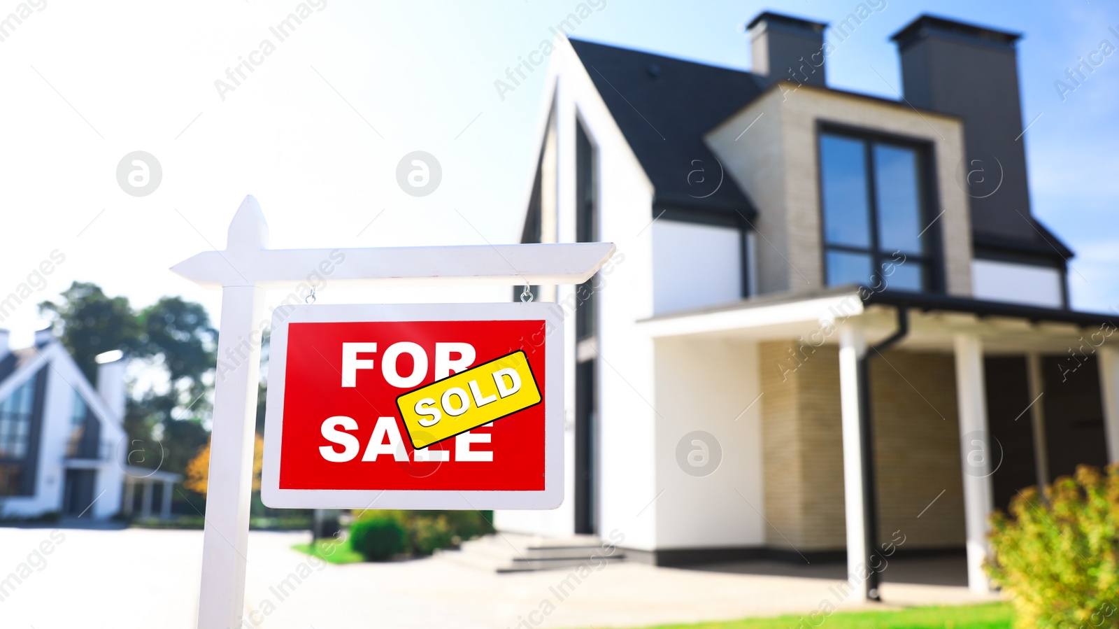 Photo of Red real estate sign near house outdoors on sunny day