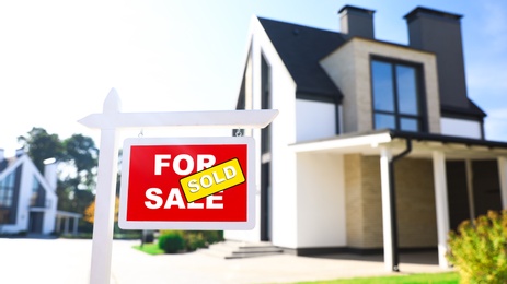 Red real estate sign near house outdoors on sunny day