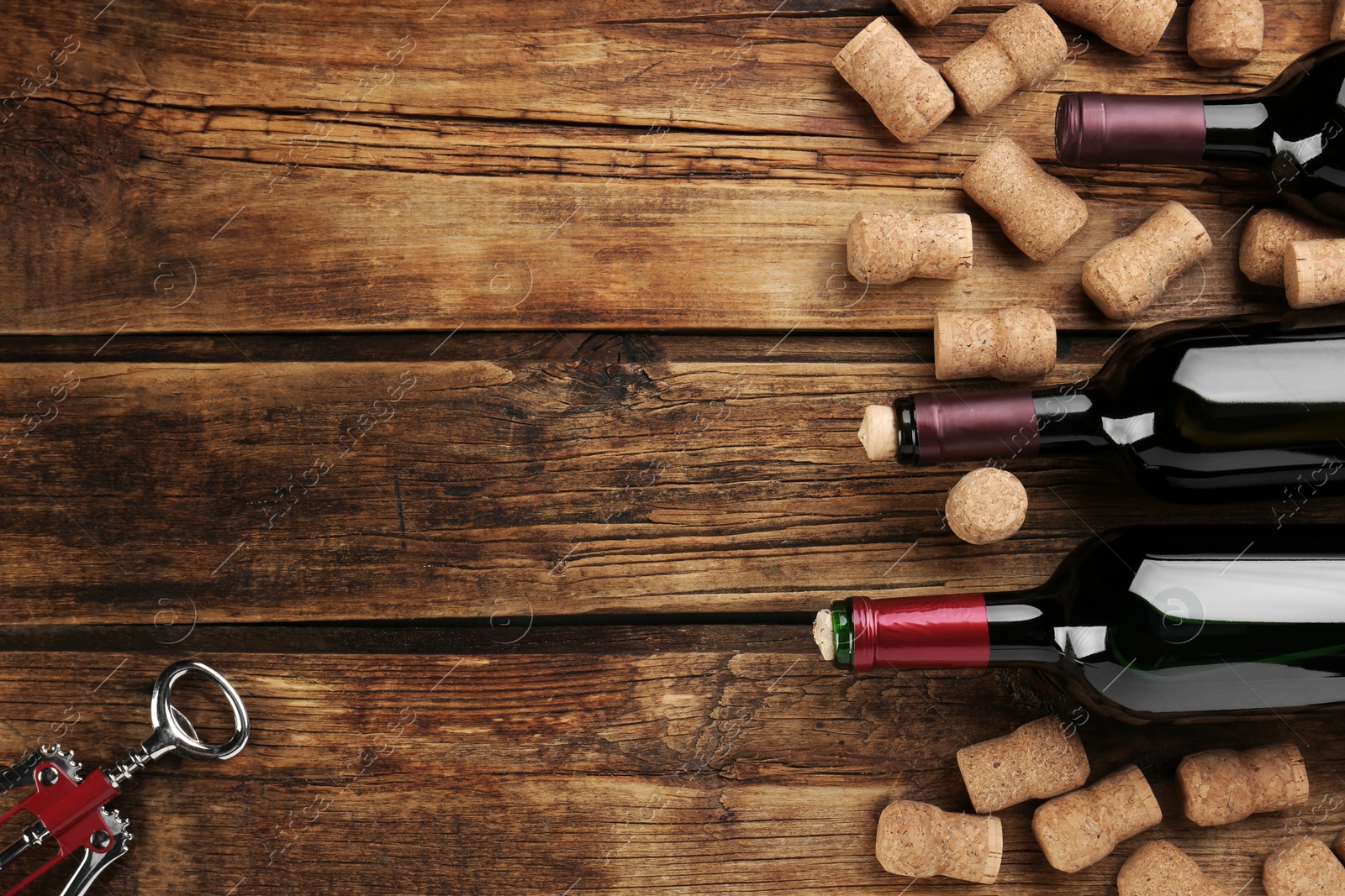 Photo of Bottles with wine, corkscrew and corks on wooden table, flat lay. Space for text