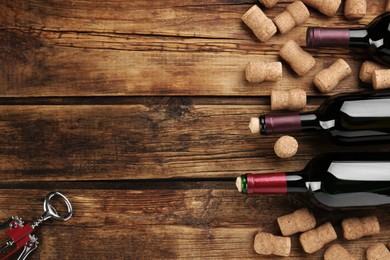 Photo of Bottles with wine, corkscrew and corks on wooden table, flat lay. Space for text
