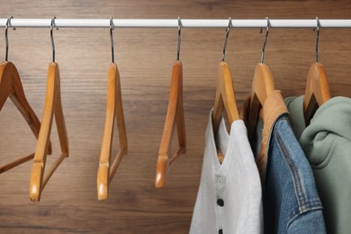 Photo of Hangers and stylish women`s clothes on rack near wooden wall, closeup