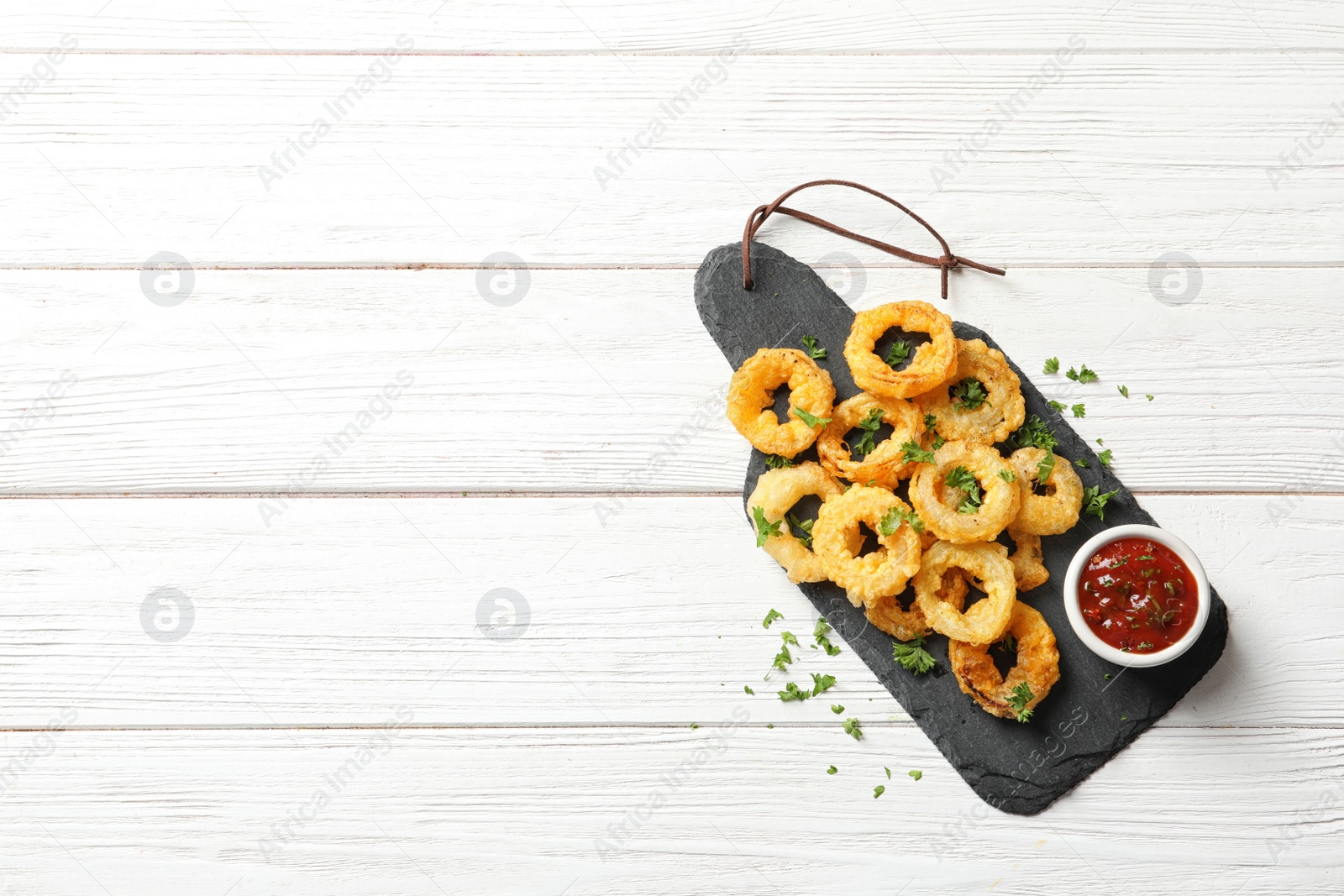 Photo of Homemade crunchy fried onion rings with tomato sauce on wooden table, top view. Space for text