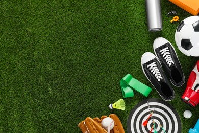 Photo of Different sport equipment and sneakers on green grass, flat lay. Space for text