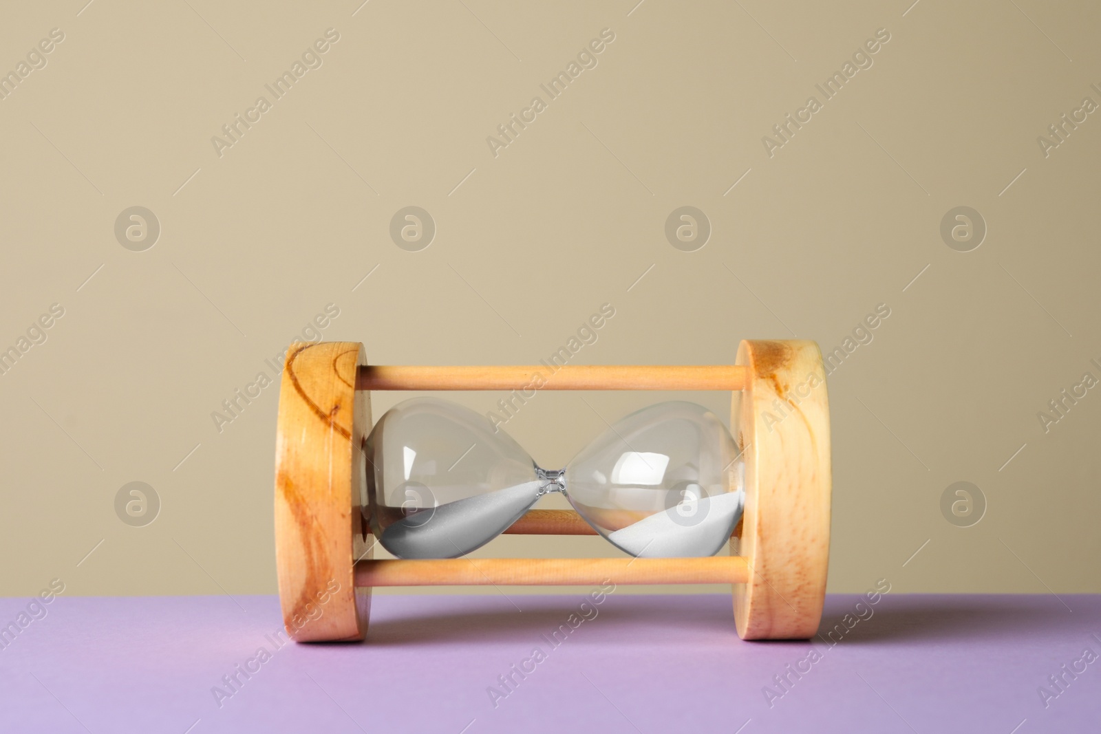 Photo of Hourglass with sand on violet table against beige background. Menopause concept