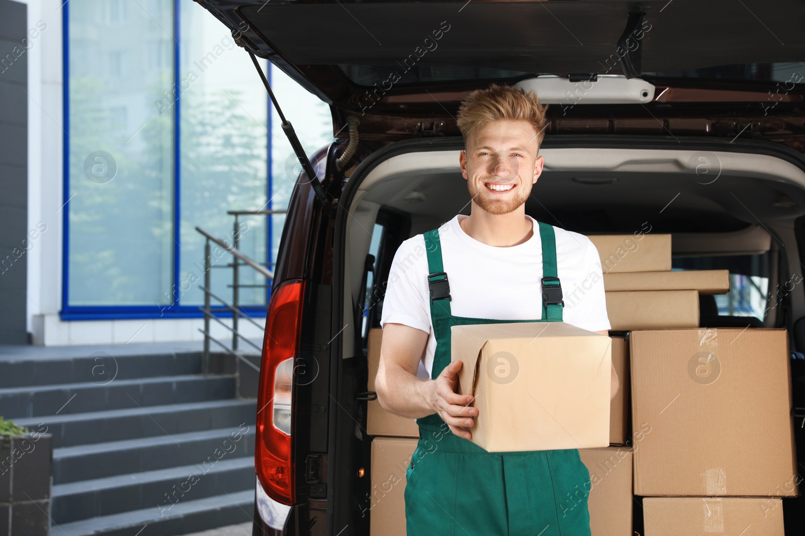 Photo of Young courier with parcel near delivery car outdoors