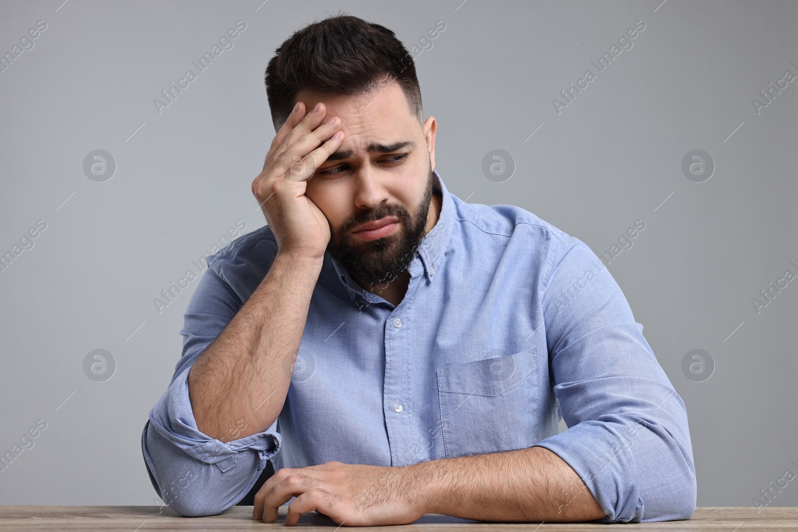 Photo of Portrait of sad man at wooden table on light grey background