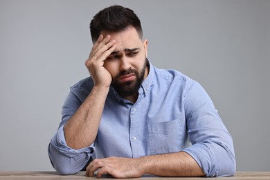 Portrait of sad man at wooden table on light grey background