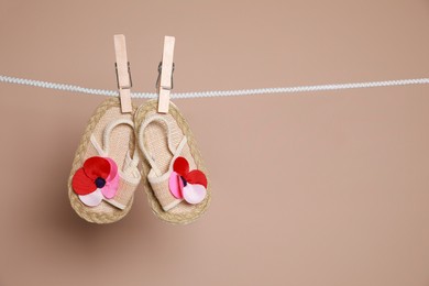 Cute small baby shoes hanging on washing line against brown background, space for text