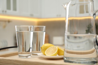 Jug, glasses with clear water and lemons on table in kitchen, closeup