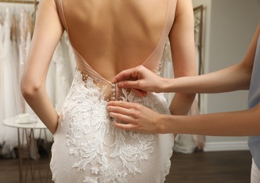 Photo of Woman helping bride wear wedding dress in boutique, closeup