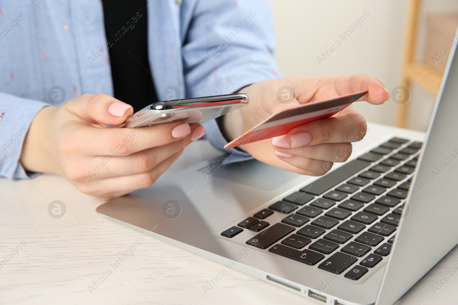 Photo of Online payment. Woman using credit card and smartphone near laptop at white wooden table indoors, closeup