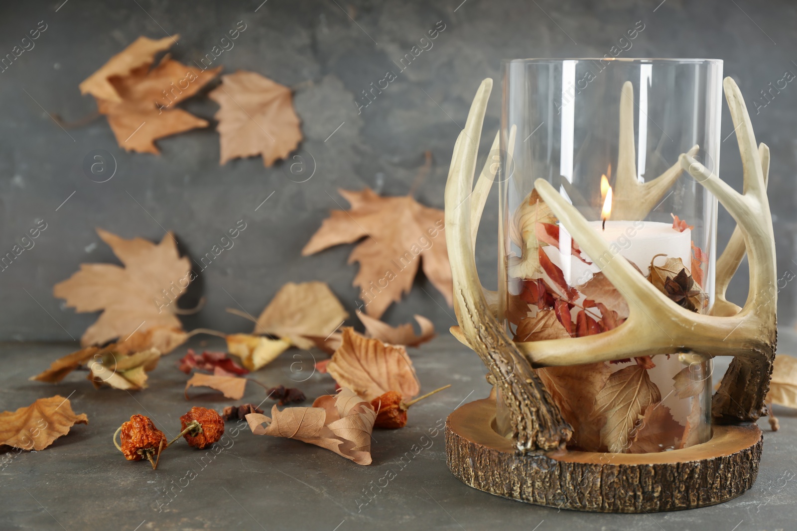 Photo of Stylish holder with burning candle and autumn decor on grey stone table. Space for text