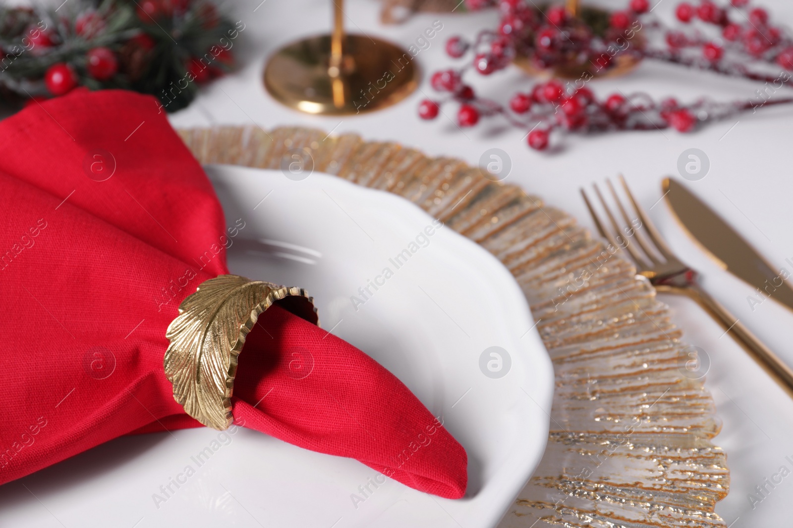 Photo of Plates and red fabric napkin with decorative ring on white table, closeup. Space for text