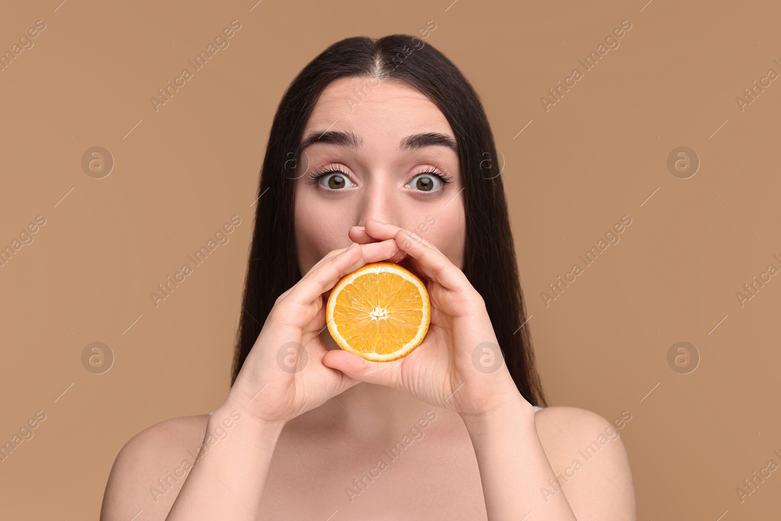 Photo of Beautiful young woman with piece of orange on beige background