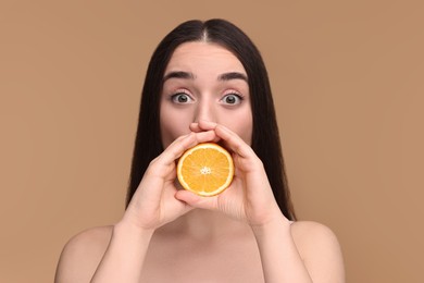 Beautiful young woman with piece of orange on beige background