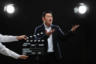 Photo of Emotional asian actor performing while second assistant camera holding clapperboard on stage. Film industry