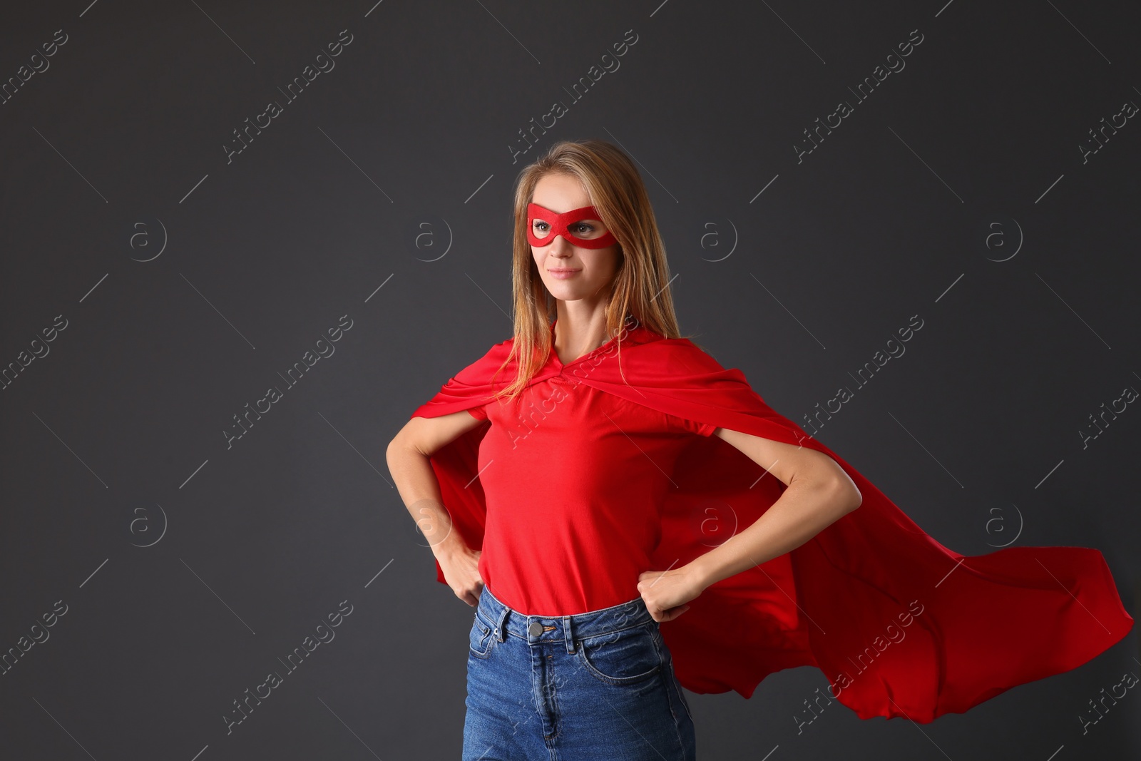 Photo of Confident woman wearing superhero cape and mask on grey background