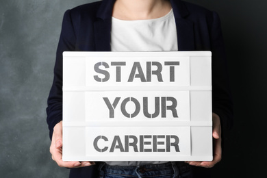 Woman holding board with words START YOUR CAREER on grey background, closeup