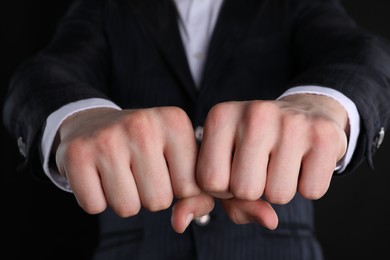 Businessman showing fists with space for tattoo on black background, closeup