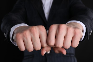 Photo of Businessman showing fists with space for tattoo on black background, closeup