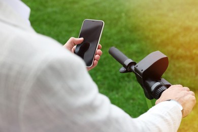 Photo of Businessman with modern kick scooter using smartphone outdoors, closeup