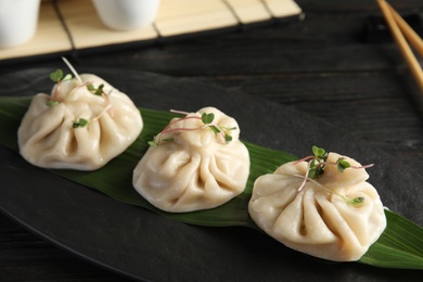 Photo of Slate plate with tasty baozi dumplings on table, closeup