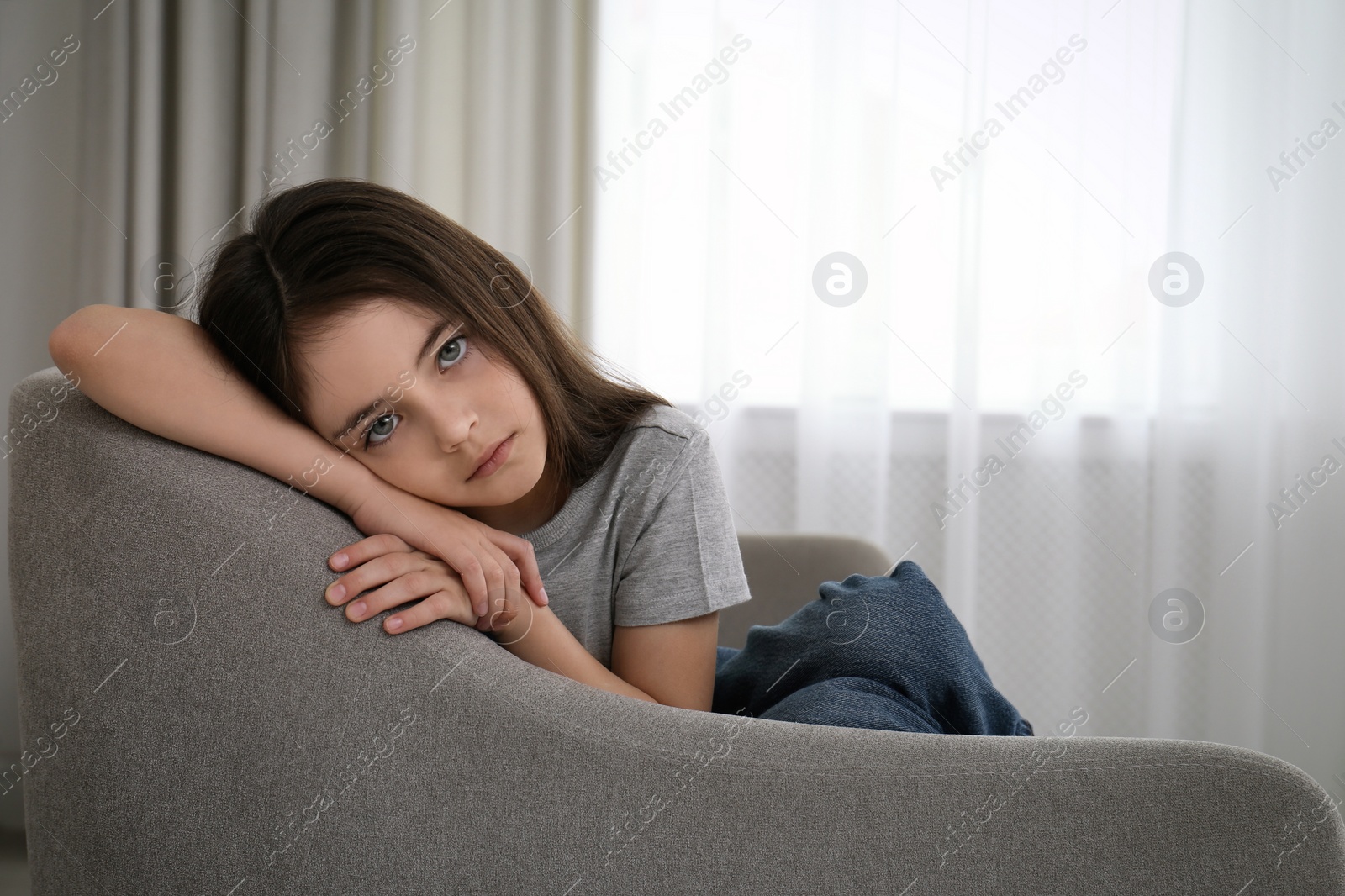 Photo of Sad little girl sitting on sofa indoors, space for text