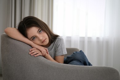 Photo of Sad little girl sitting on sofa indoors, space for text