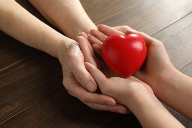 Young and elderly women holding red heart at wooden table, closeup