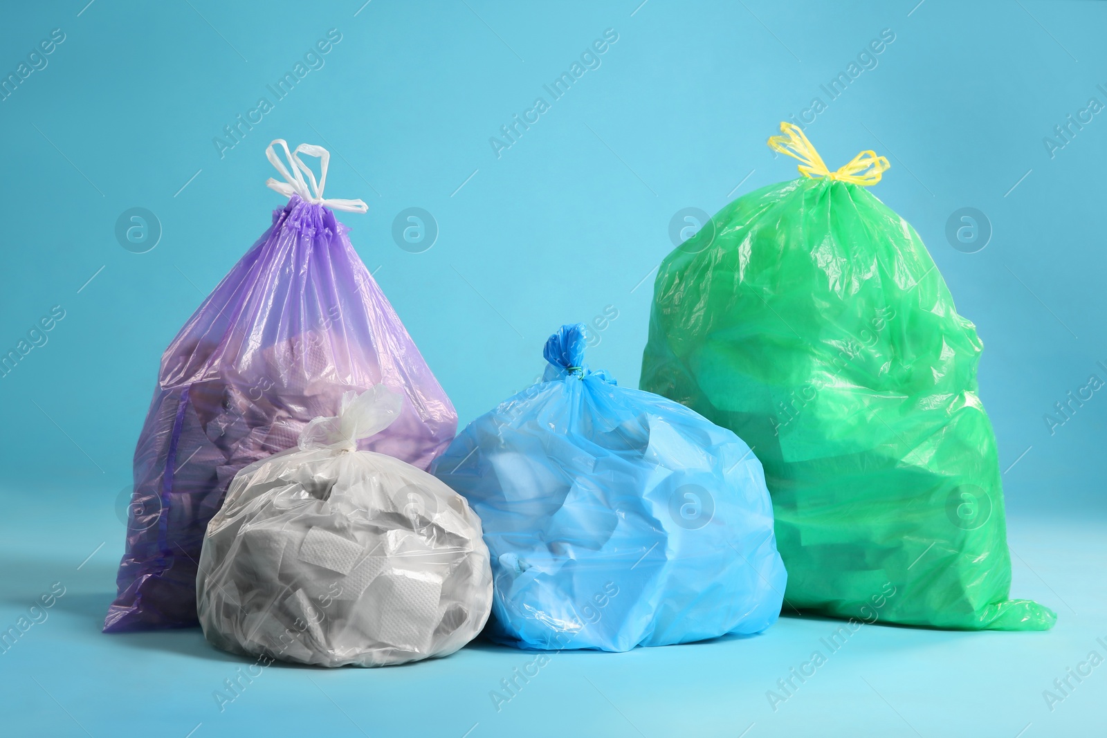 Photo of Different trash bags full of garbage on light blue background