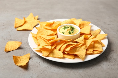 Photo of Plate with delicious mexican nachos chips and cheese sauce on grey table