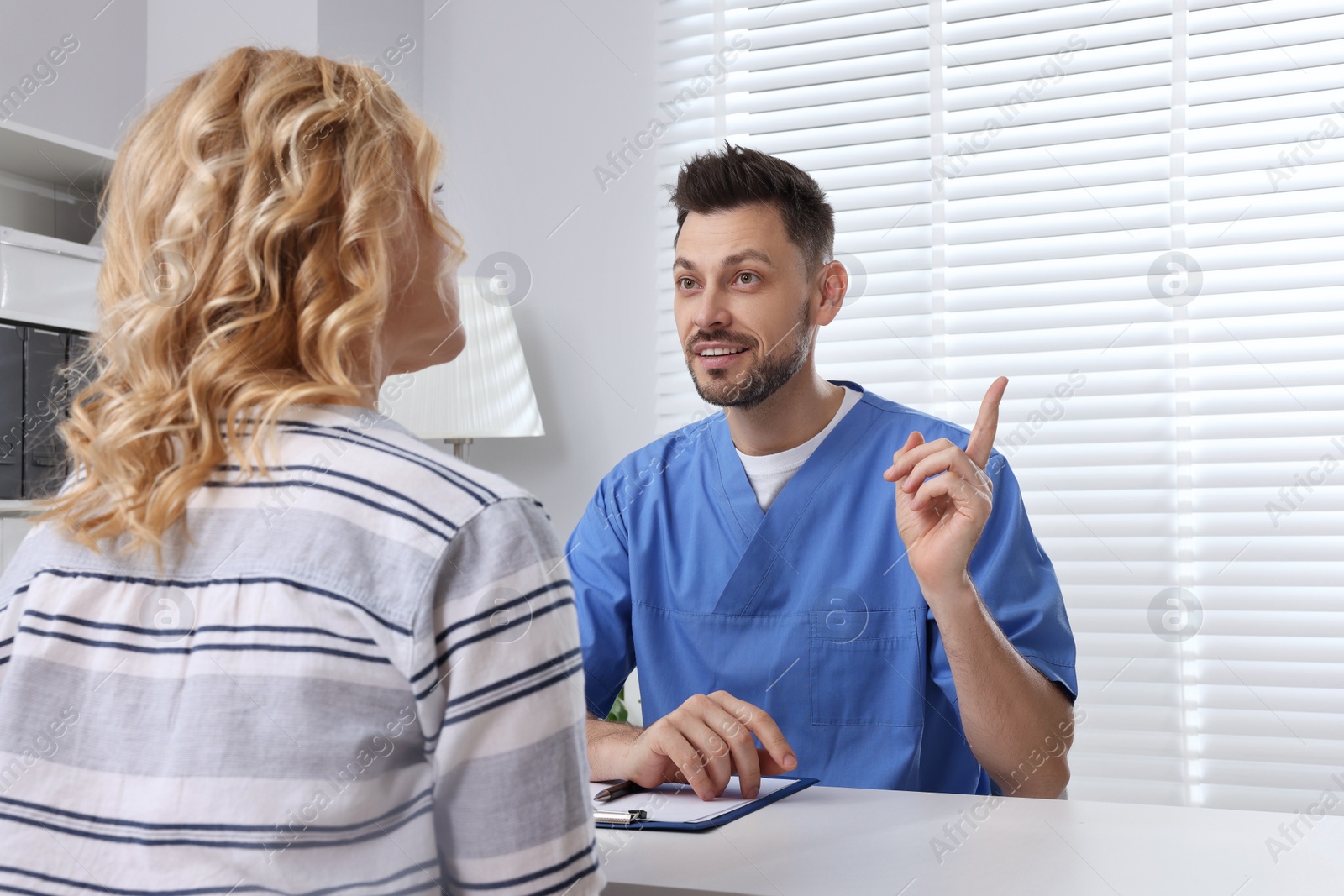 Photo of Doctor with clipboard consulting patient in clinic