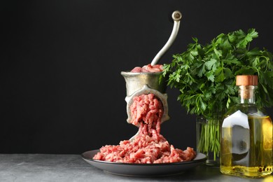 Manual meat grinder with beef mince, oil and parsley on grey table, space for text