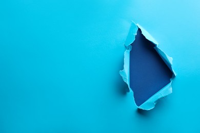Photo of Hole in light blue paper on color background, space for text