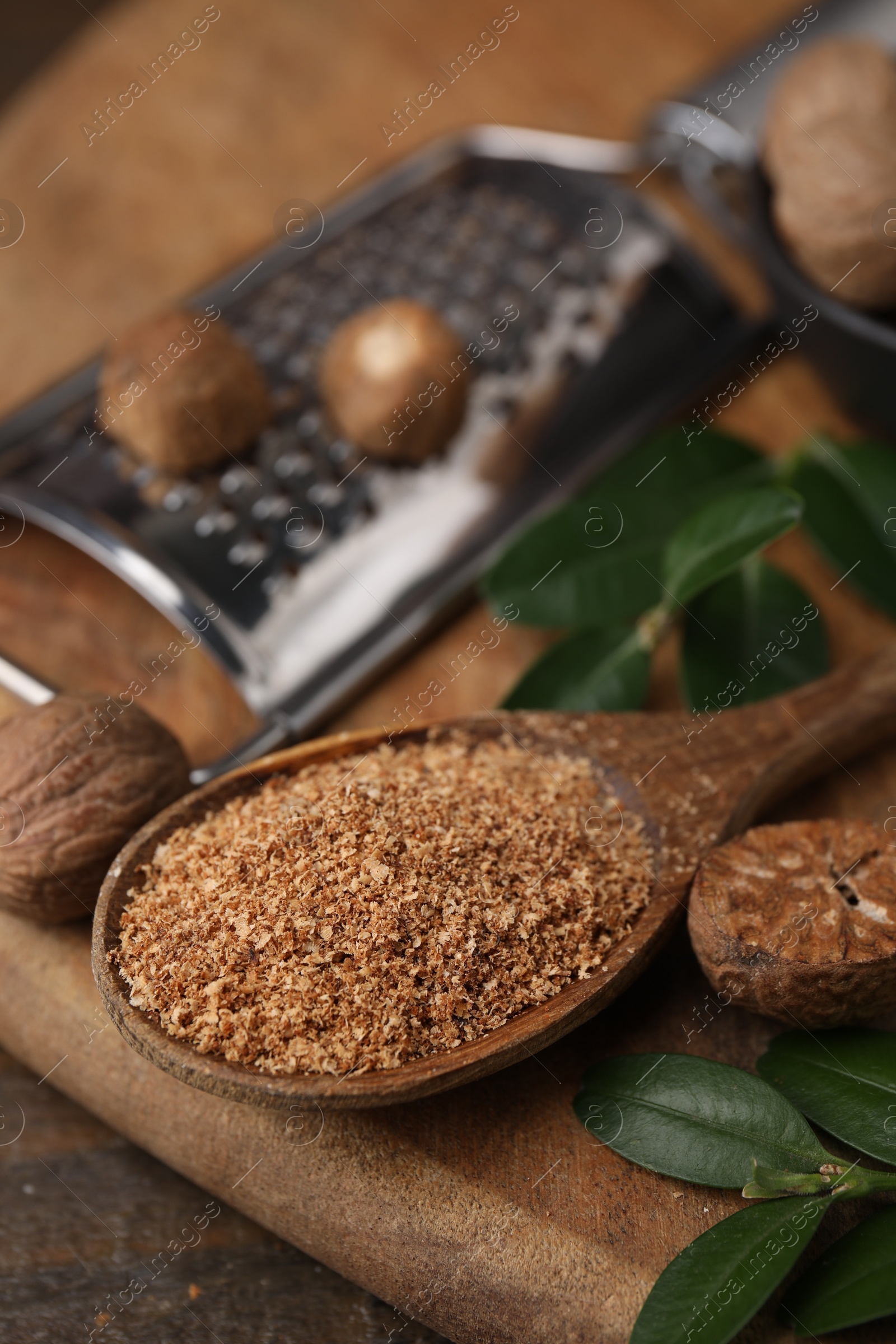 Photo of Spoon with grated nutmeg and green leaves on wooden table, closeup