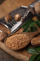 Spoon with grated nutmeg and green leaves on wooden table, closeup