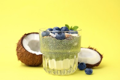 Photo of Tasty chia matcha pudding with coconut and blueberries on yellow background. Healthy breakfast