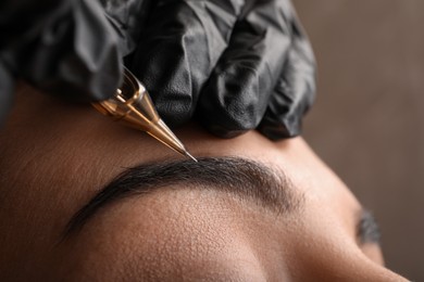 Young woman undergoing procedure of permanent eyebrow makeup in tattoo salon, closeup