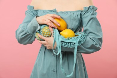 Photo of Woman with string bag of fresh lemons on pink background, closeup