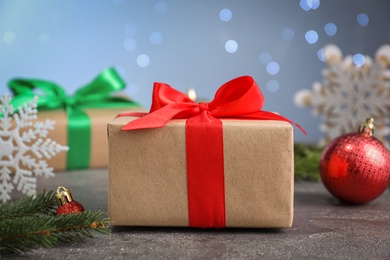 Photo of Christmas gift box with red ribbon and festive decor on grey table against blurred lights, closeup
