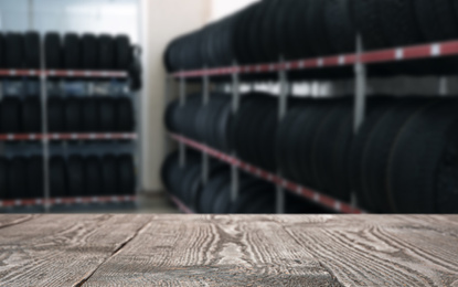 Empty wooden surface and blurred view of car tires in auto store, closeup. Space for text 