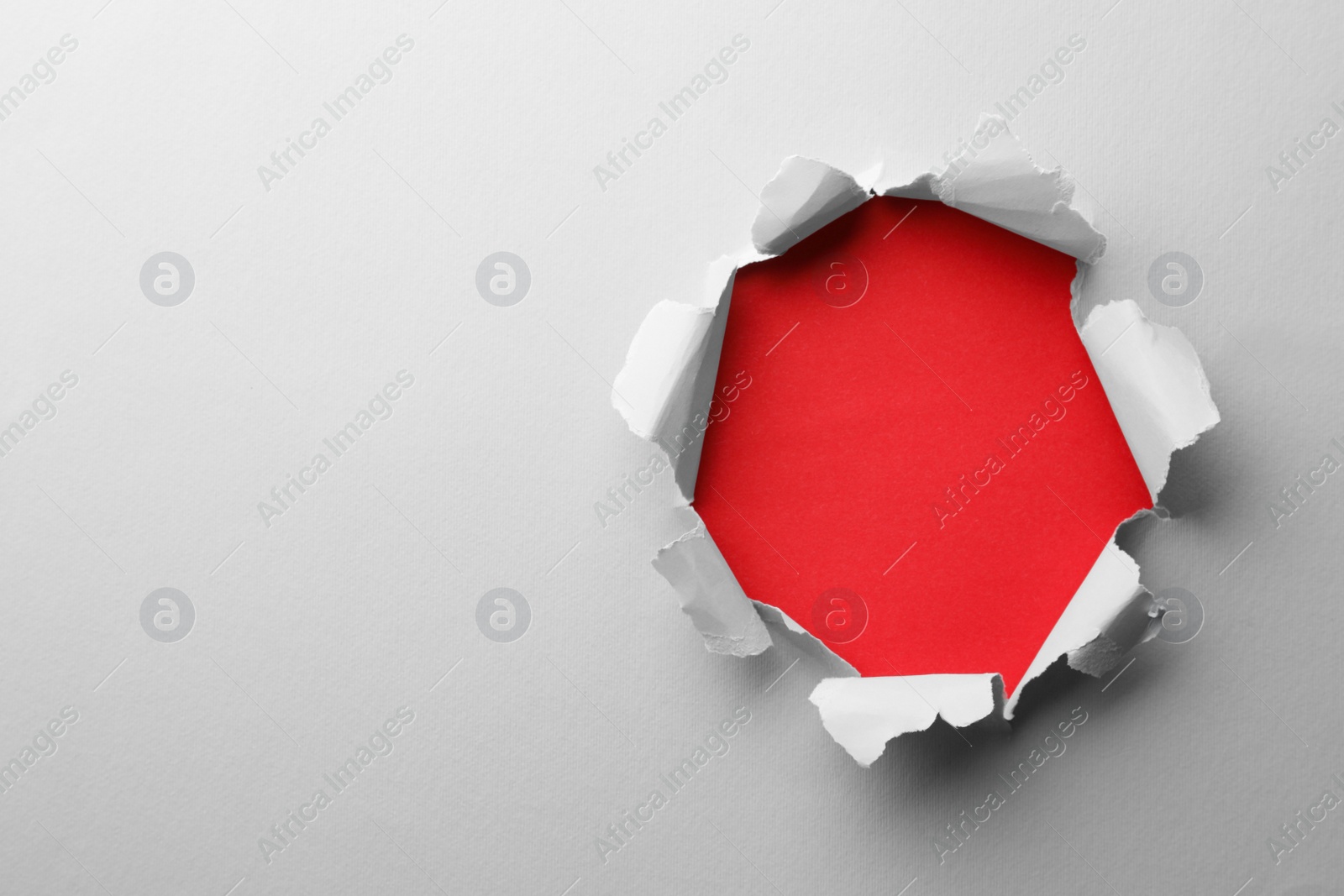 Photo of Hole in white paper on red background, space for text