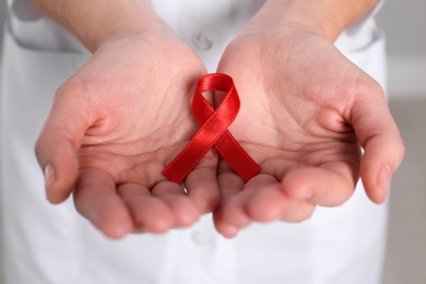 Photo of Woman holding red awareness ribbon, closeup. World AIDS disease day